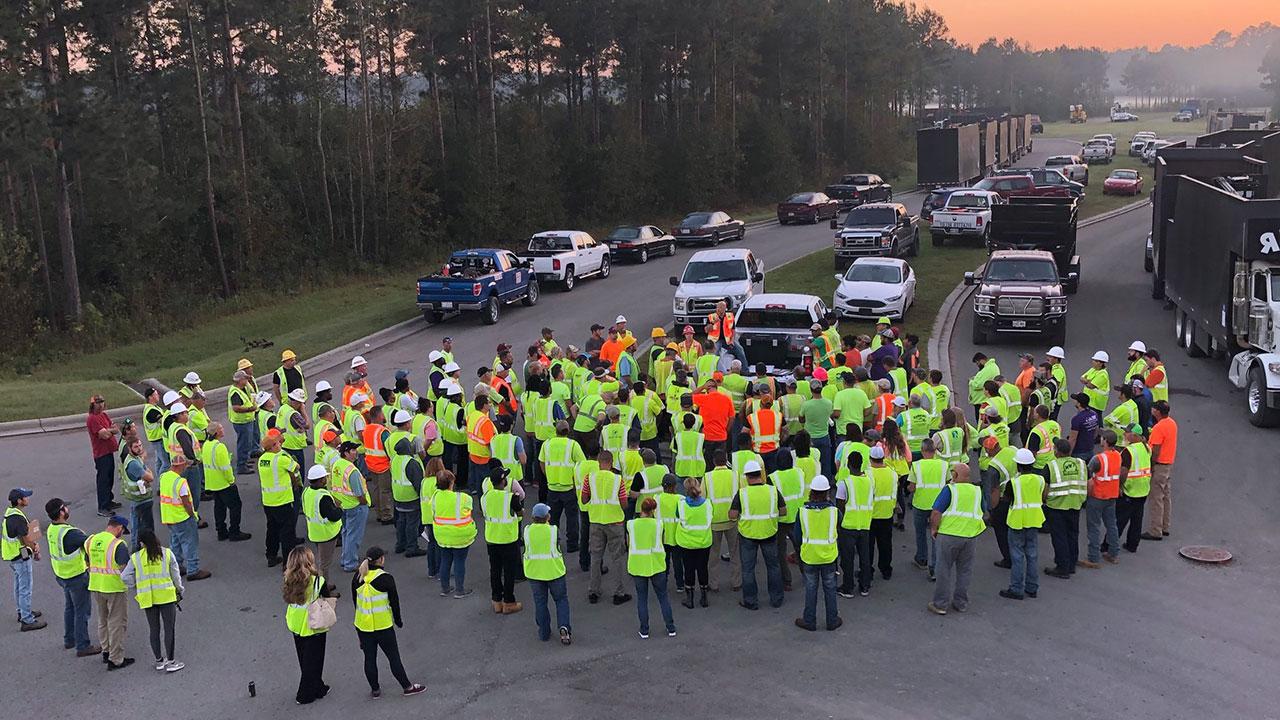 一群现场工作全球最大体育平台员站在路上, 穿着背心和安全帽, 被工作卡车包围